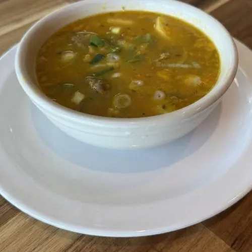 A bowl of Jamaican soup with meat, dumplings and scallions