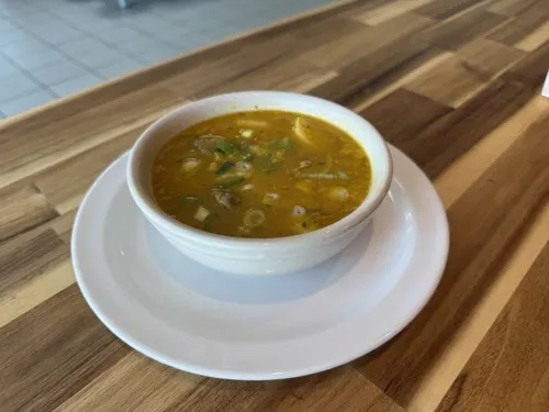 A bowl of Jamaican soup with meat, dumplings and scallions